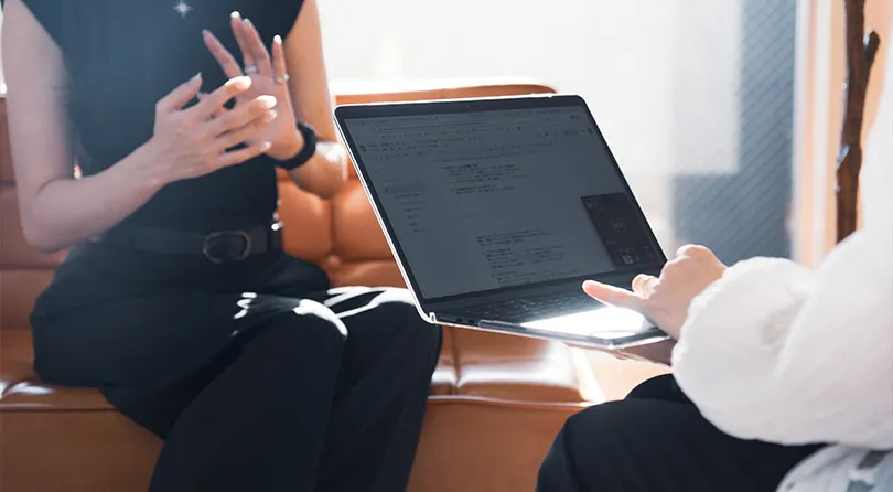 ソファに座った人物と、膝の上にノートパソコンを置いた人物が向かい合っている写真