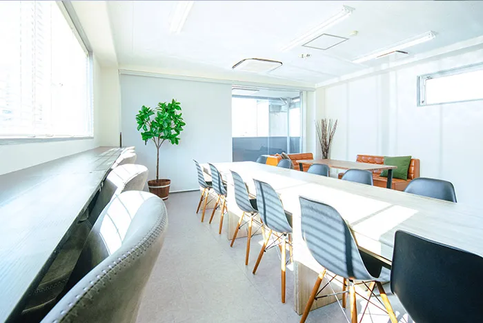 長いテーブルと複数の椅子が並んでいる会議スペース。白い壁と大きな窓に囲まれた明るい空間。